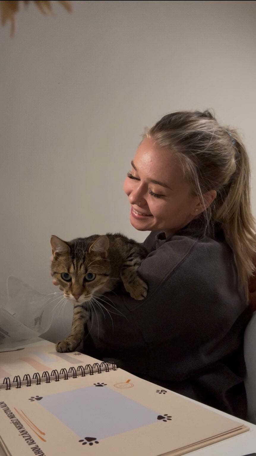 Mosolygó lány gazdi mutatja az ülében bújó macskájának a kinyitott Cicanaplót.