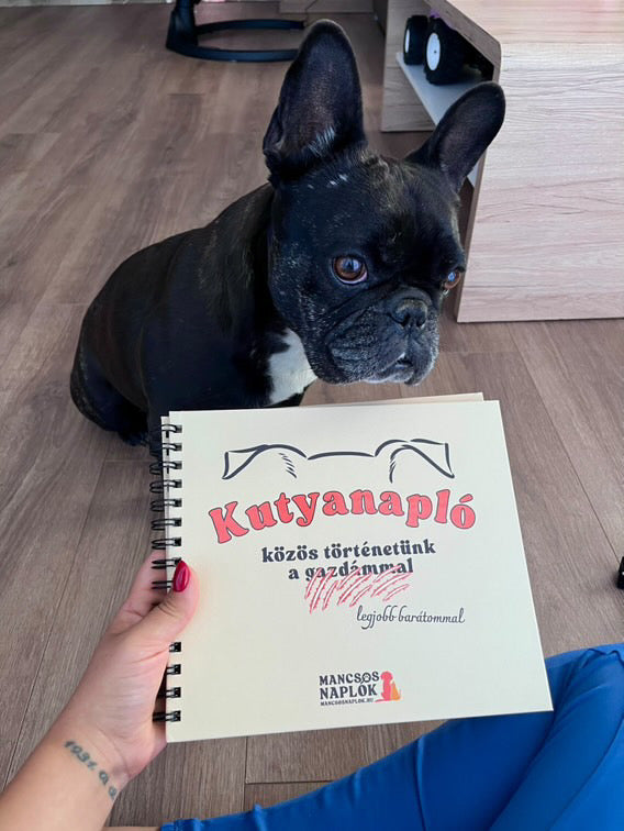 Kutyanapló a Mancsos Naplók sorozat részeként, mögötte egy kutya ül és néz a gazdájára, aki tartja a naplót.