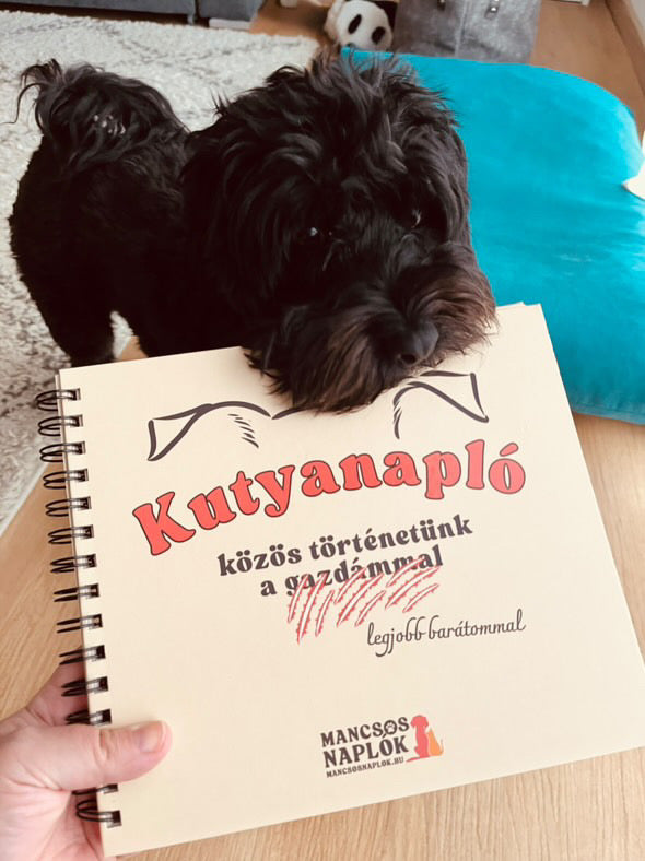 Kutyanapló a Mancsos Naplók sorozat részeként, mögötte egy kutya áll és mintha ráharapna a naplóra.
